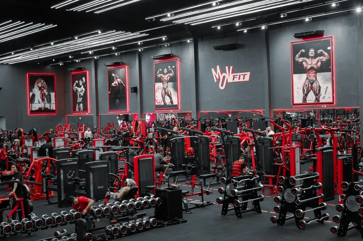 Vista ampla do piso de treino da academia MOVFIT com equipamentos profissionais e iluminação em vermelho